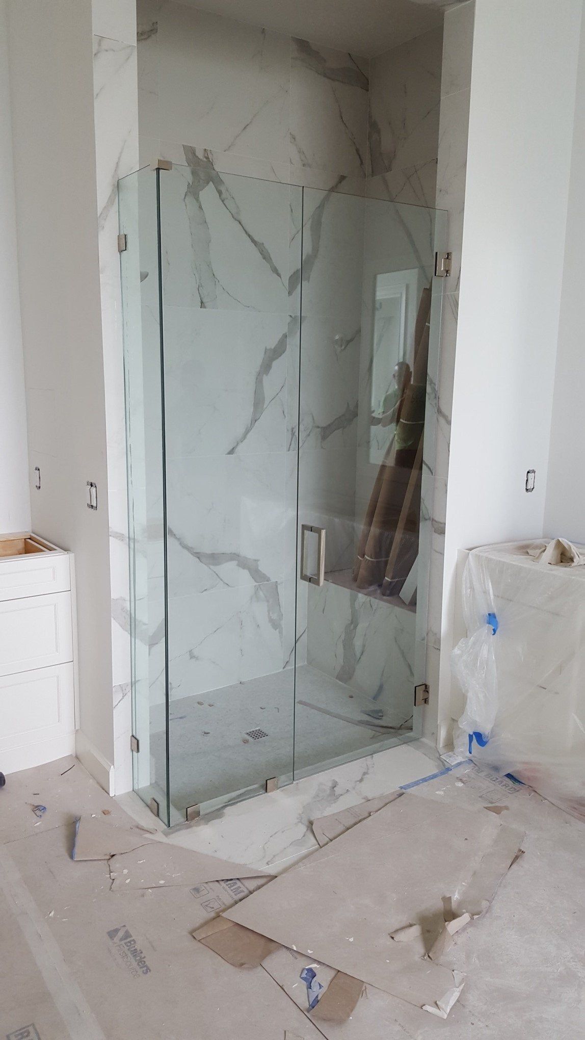 Walk-in shower with glass door and marble-pattern tile in an unfinished bathroom.