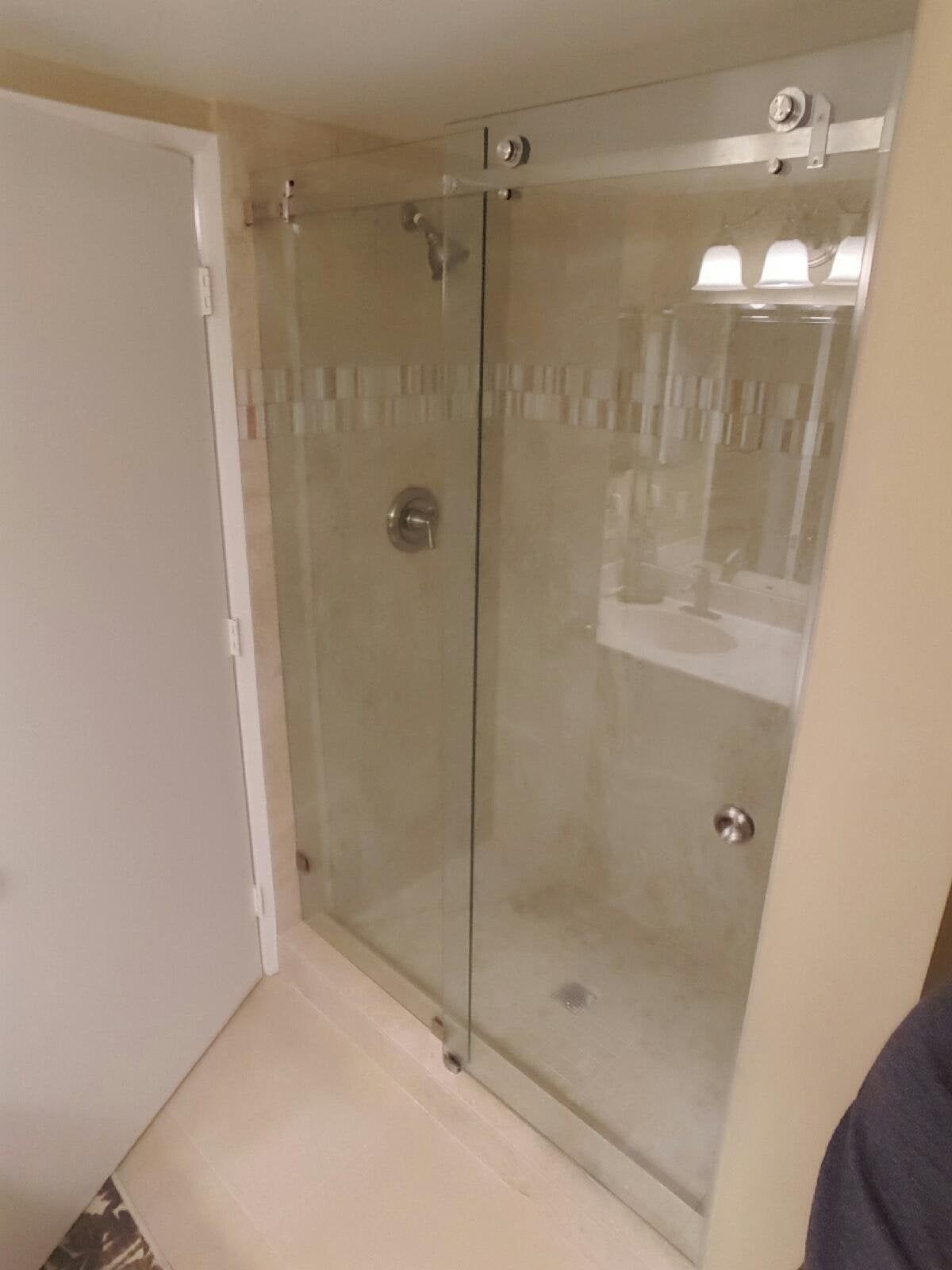 Glass shower enclosure with sliding doors and beige bathroom walls