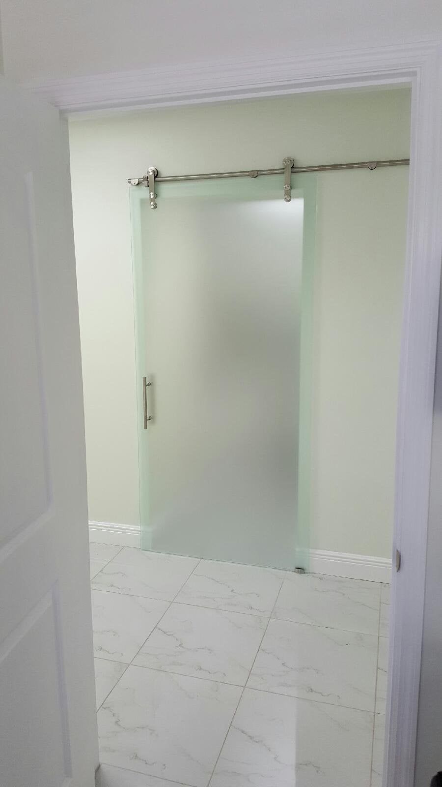 Empty tiled room with frosted glass sliding door and metal track overhead