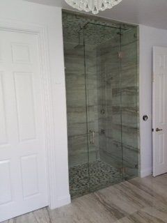 Modern bathroom shower with glass enclosure, white walls, and gray wood-look floor.