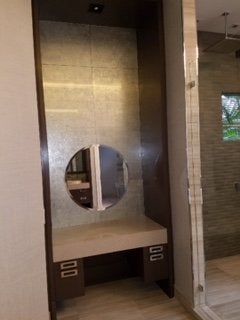 Built-in vanity nook with circular mirror and dark wood shelving, in a tiled interior room