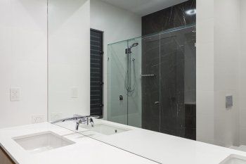 Modern white bathroom vanity with sink, large mirror, and glass-enclosed shower with dark tile flooring