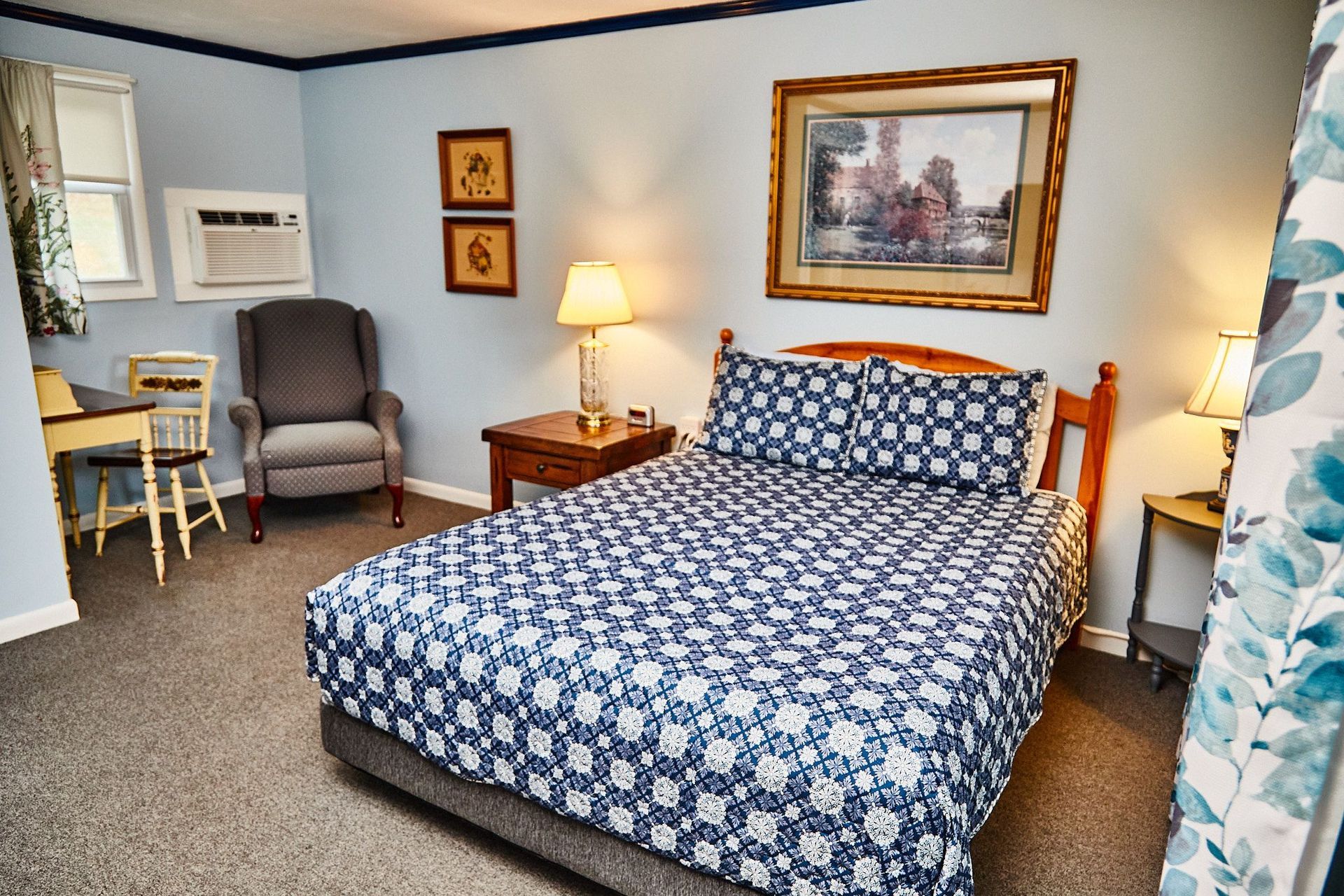 a hotel room with a king size bed , chair , desk and air conditioner .