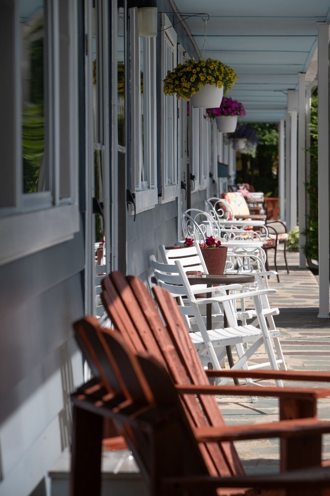 a row of chairs and tables on a porch with flowers hanging from the ceiling .