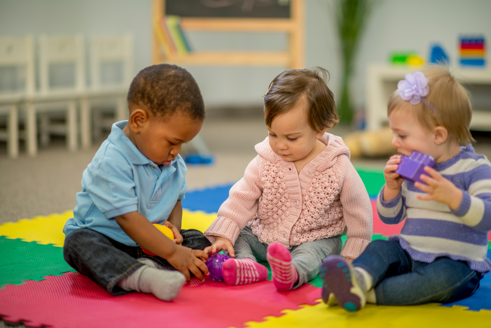 Three babies are sitting on the floor playing with toys.