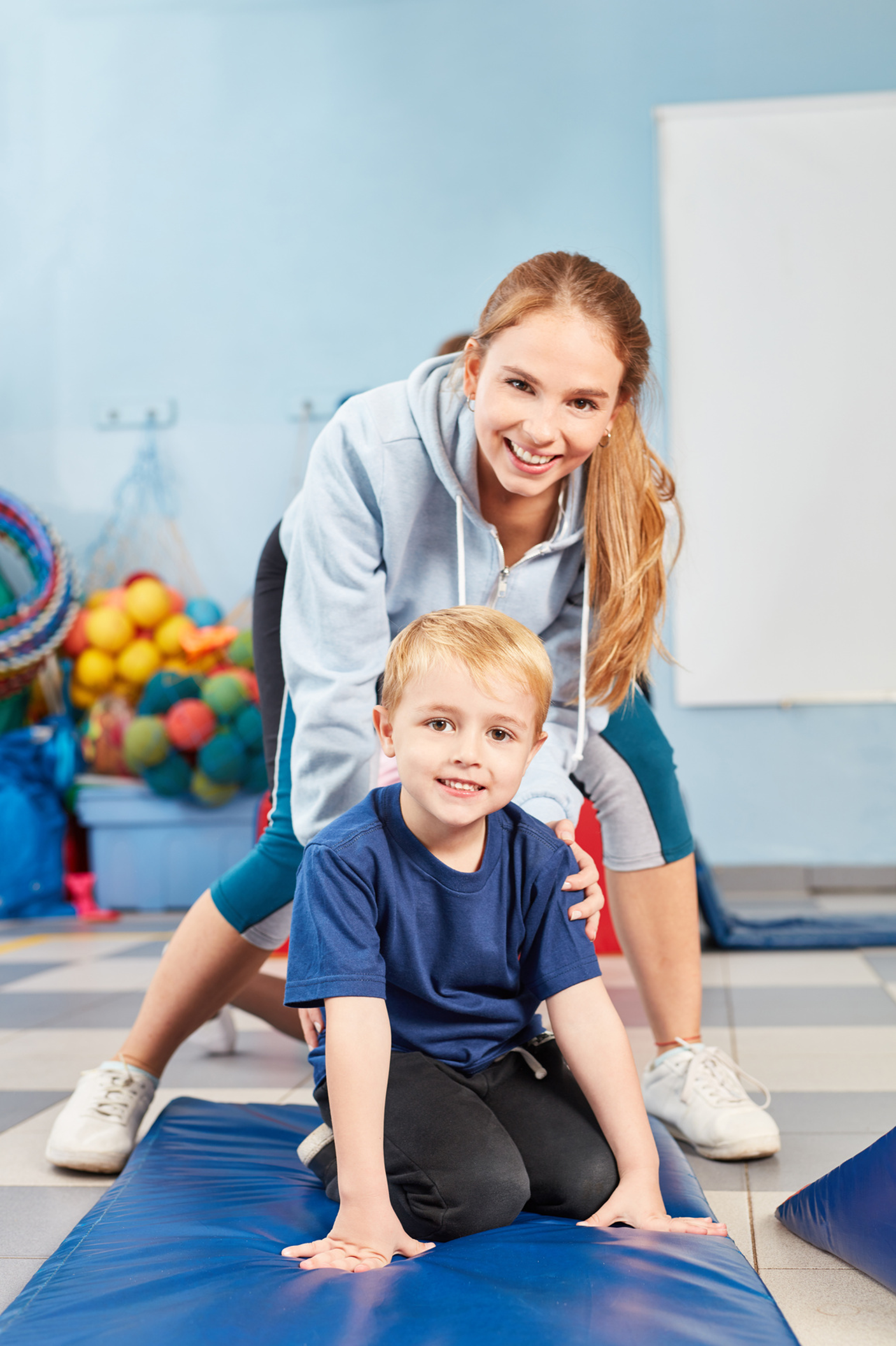 A woman is playing with a young boy on a mat in a gym.