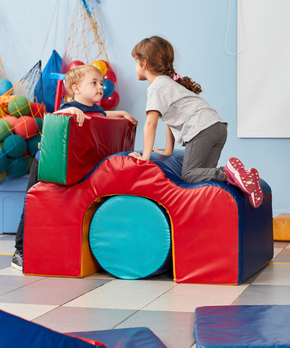 Two children are playing with foam blocks in a gym.