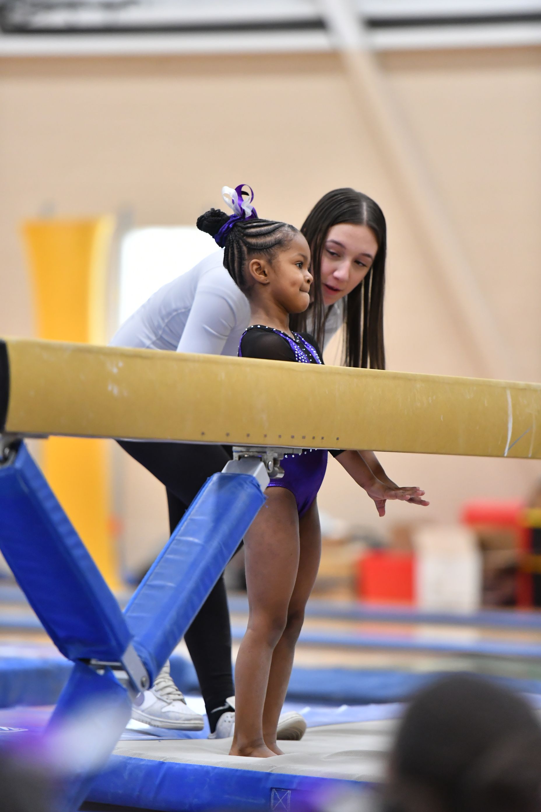 A woman is helping a little girl balance on a balance beam.