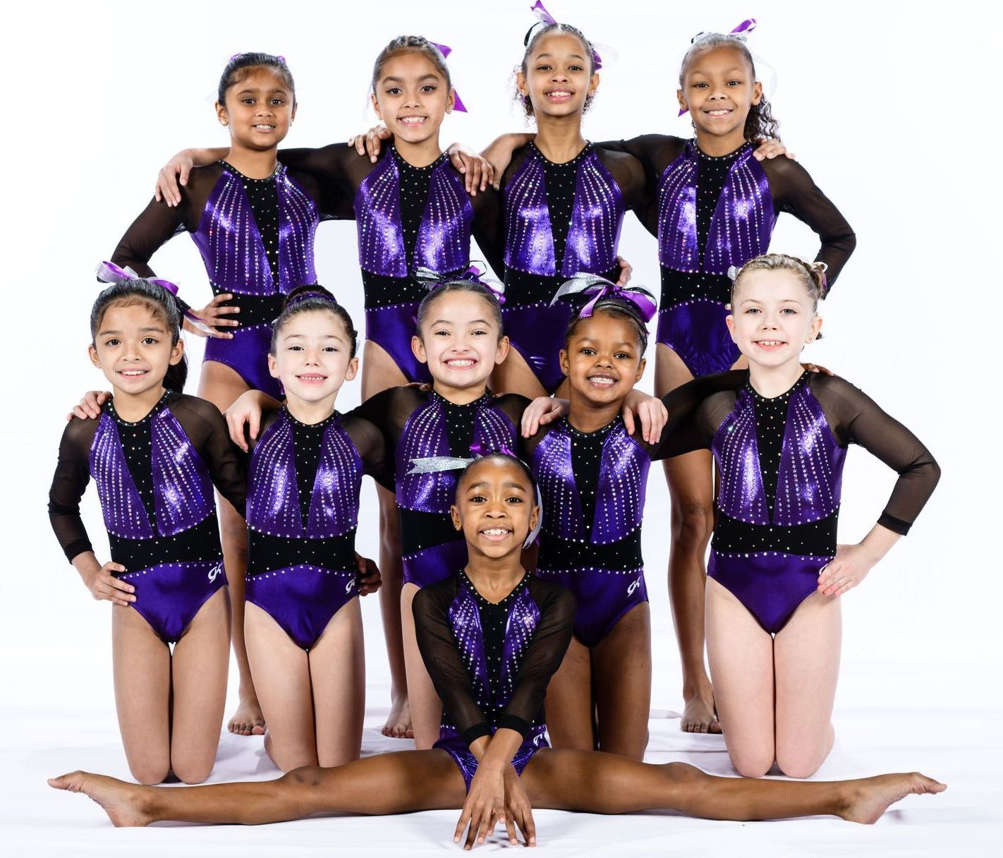 A group of young girls in purple leotards are posing for a picture.
