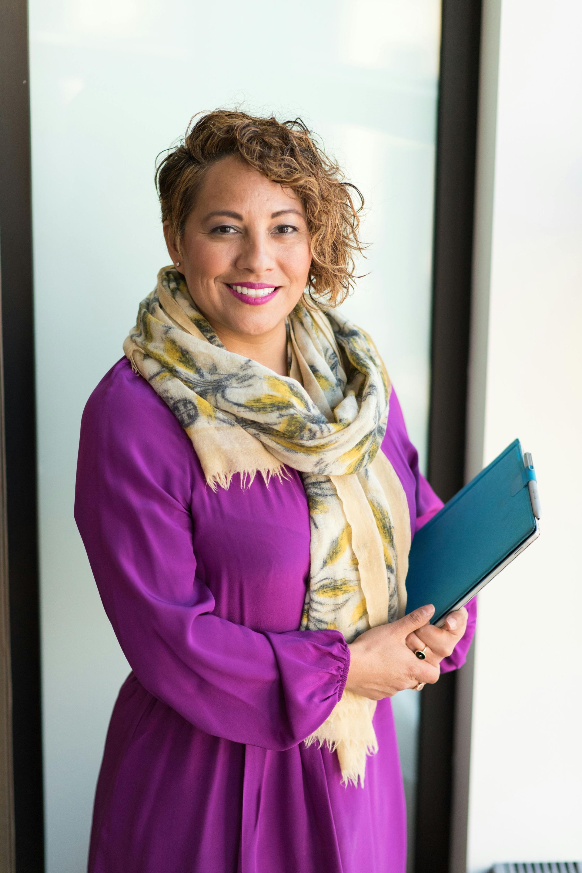 A woman in a purple dress and scarf is holding a blue folder.