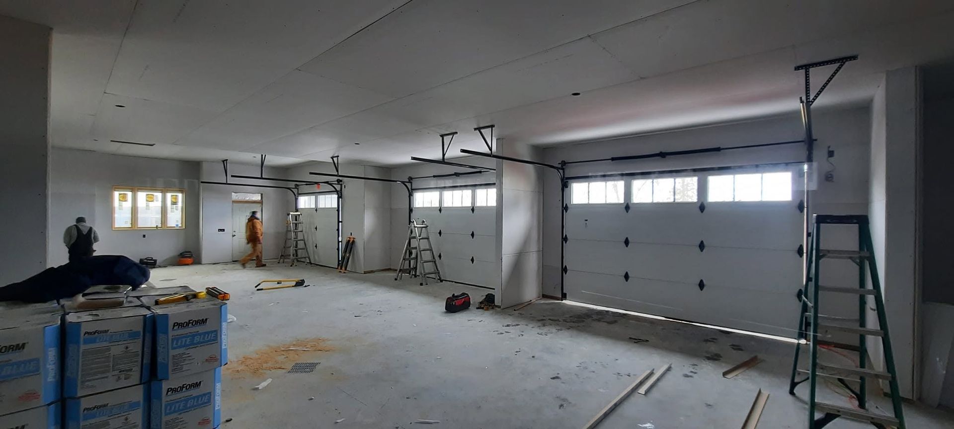 Empty garage under renovation with scattered tools, drywall debris, and a closed garage door