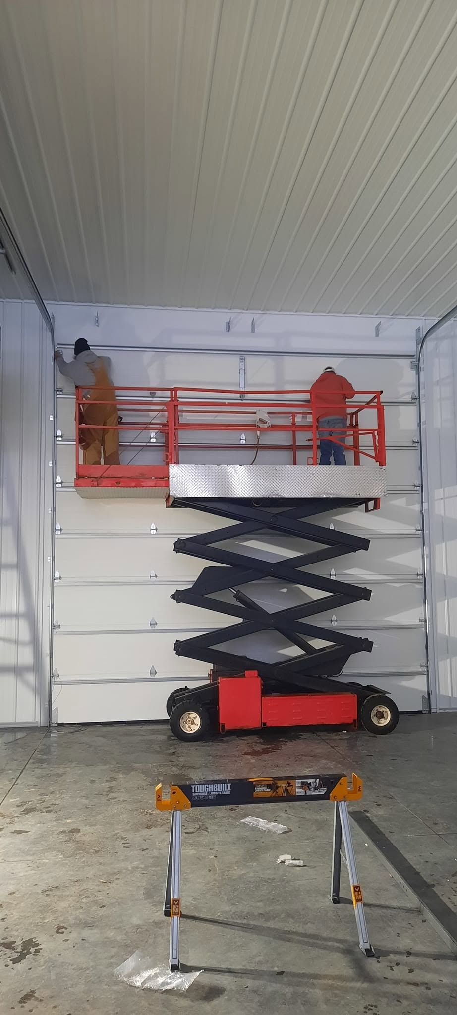 Scissor lift raised near a garage ceiling, with orange rails and a small work platform below.