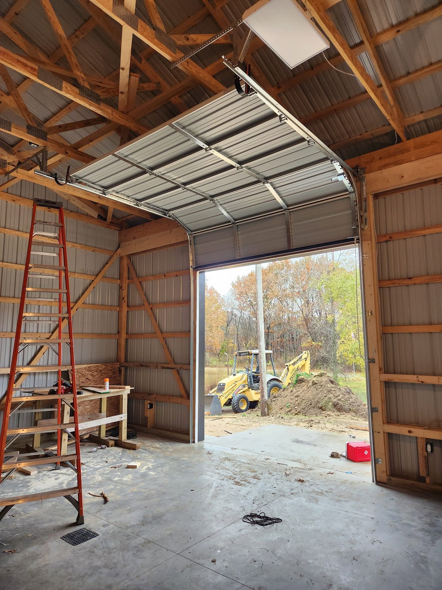 Construction site inside a garage with open door, ladders, tools, and exposed wooden roof framing