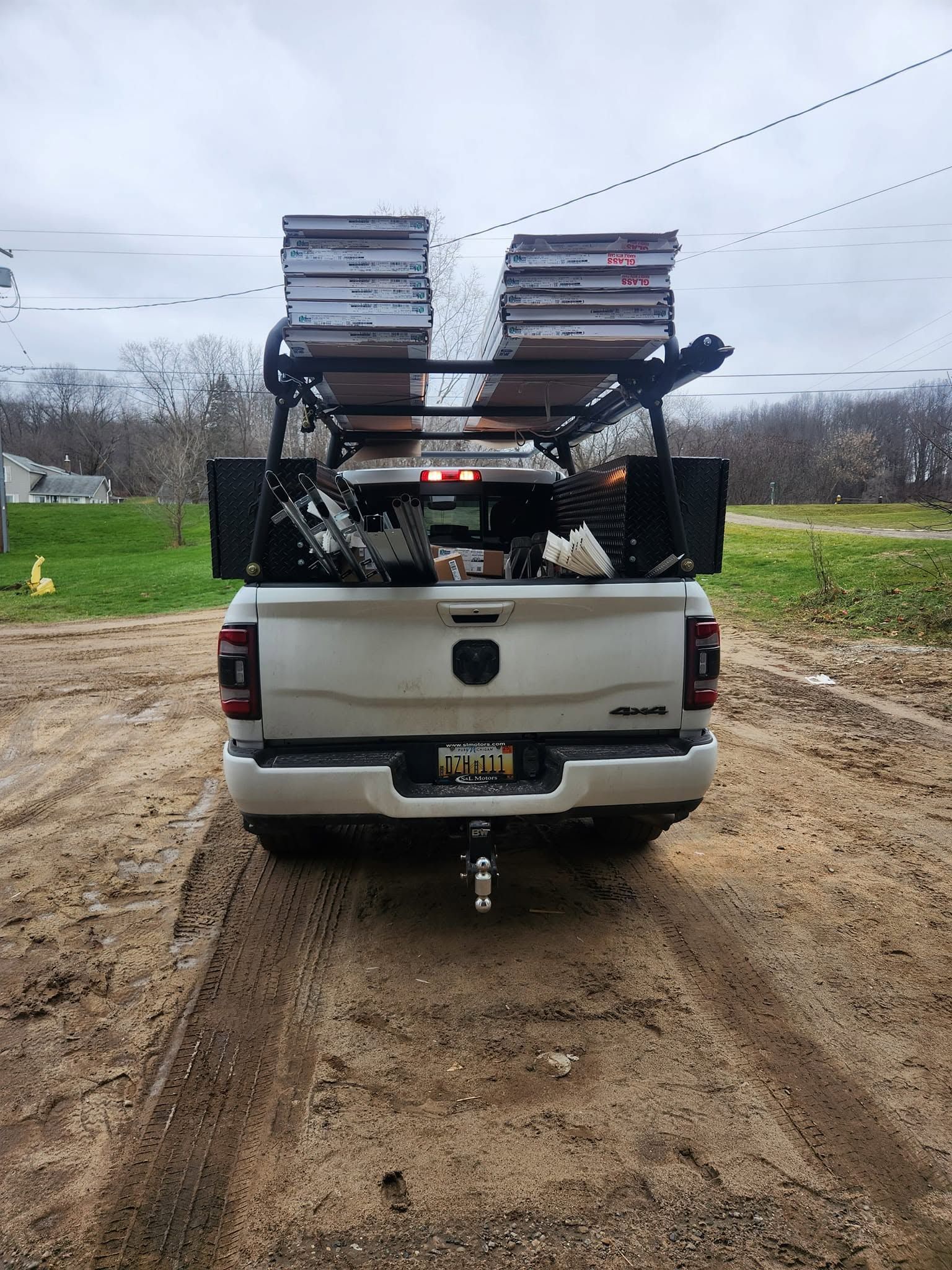 White pickup truck carrying stacked folding chairs on the back, parked on a muddy dirt road under cloudy sky