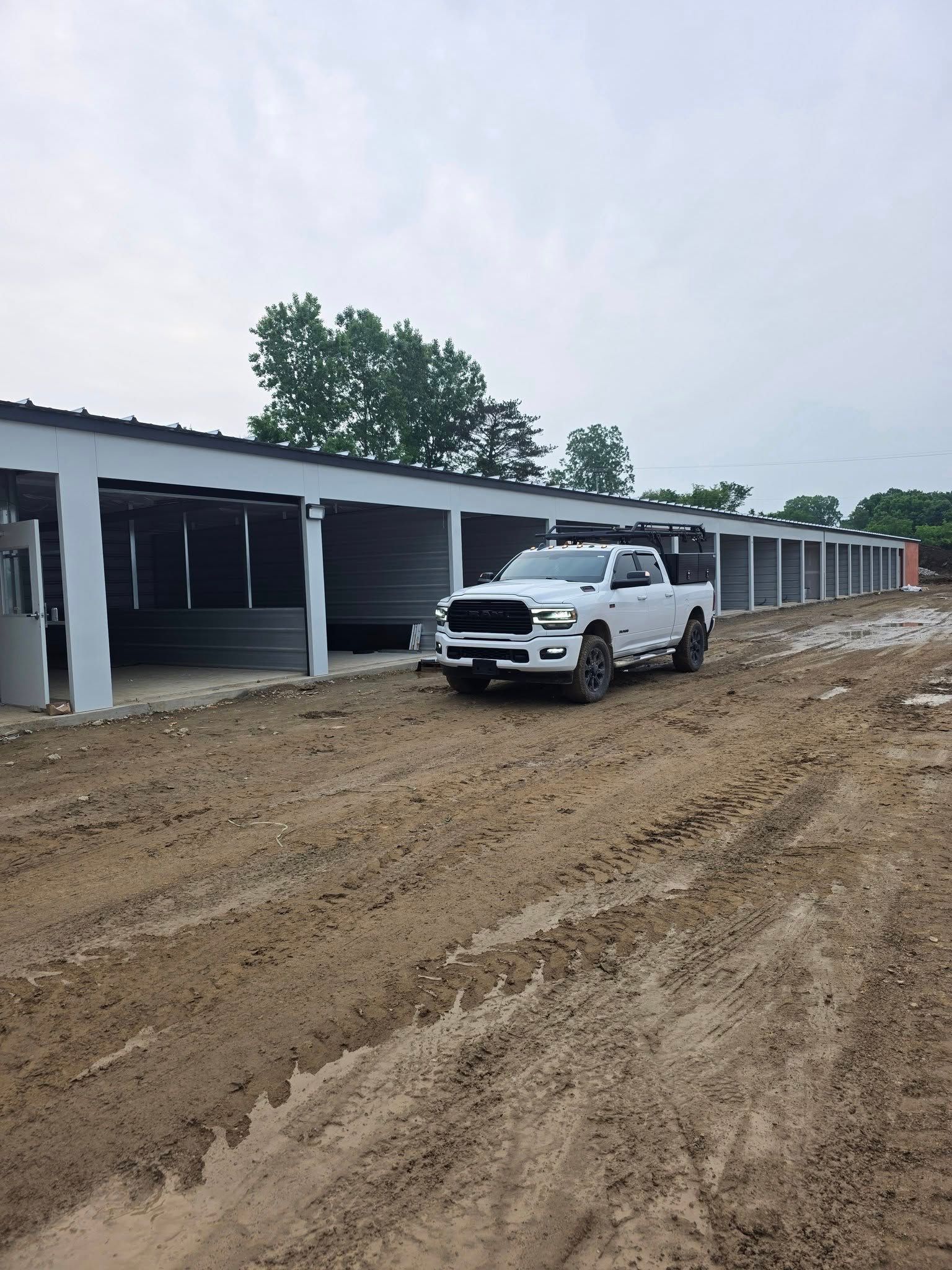 White pickup truck on a muddy road beside a row of open garage units under construction