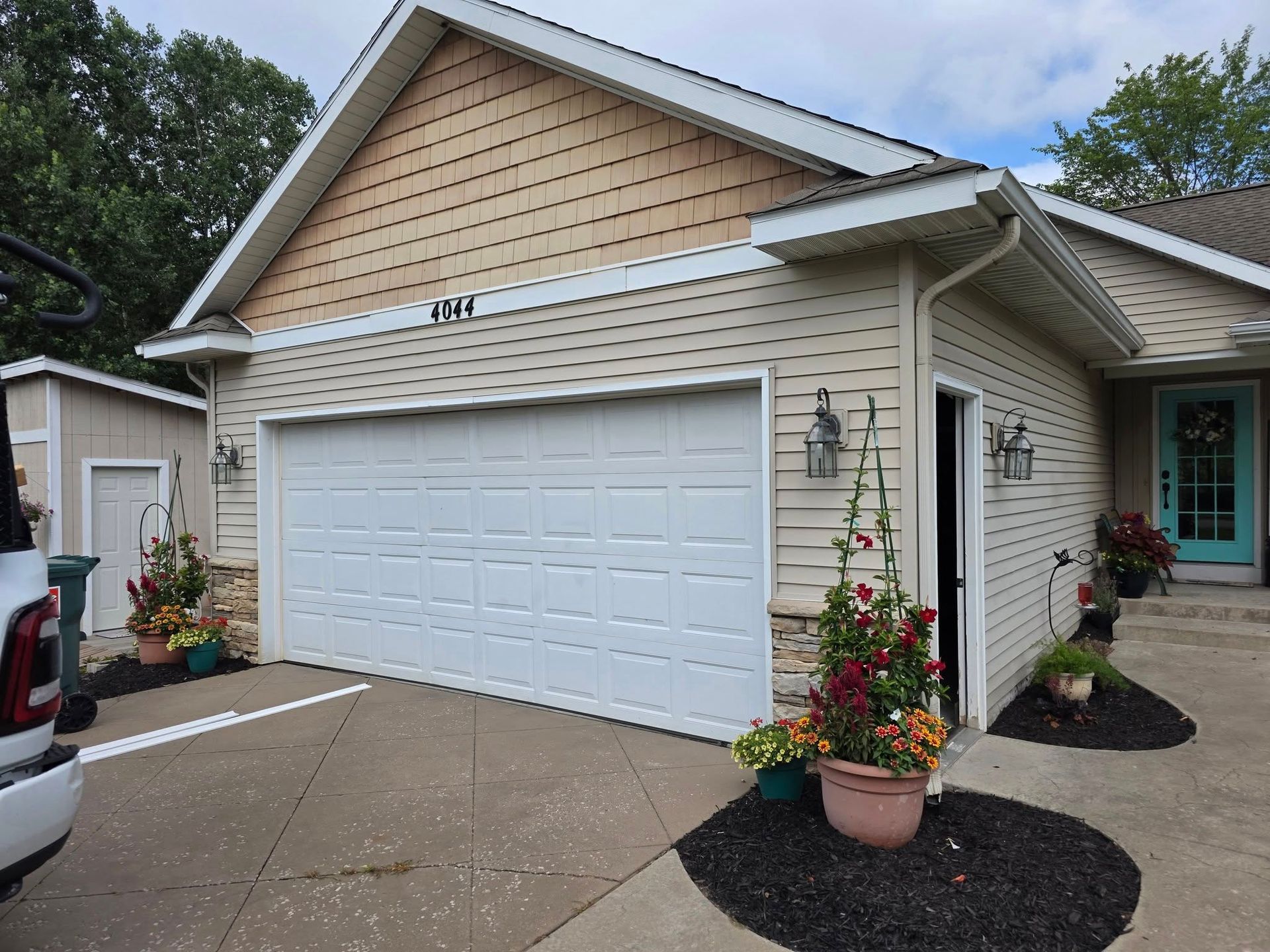 Suburban house with white garage door, beige siding, and potted flowers by the driveway