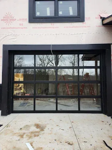 Black-framed glass sliding doors on a construction site with a window above and unfinished wall.