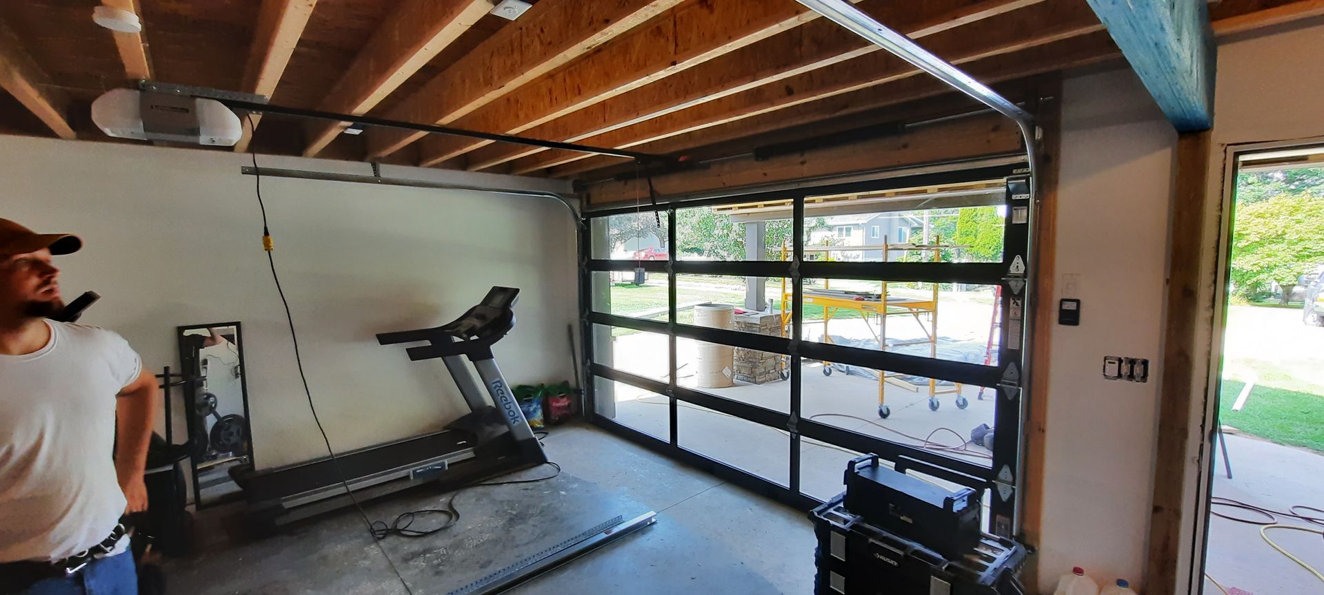Home gym with treadmill and weight bench in a garage, with large open doors to outside.