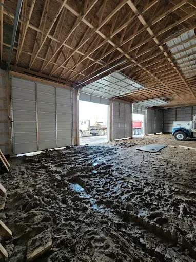 Muddy warehouse interior with exposed roof beams and an open bay door letting in daylight