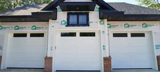 Front view of a house with three white garage doors and dark gray roof trim