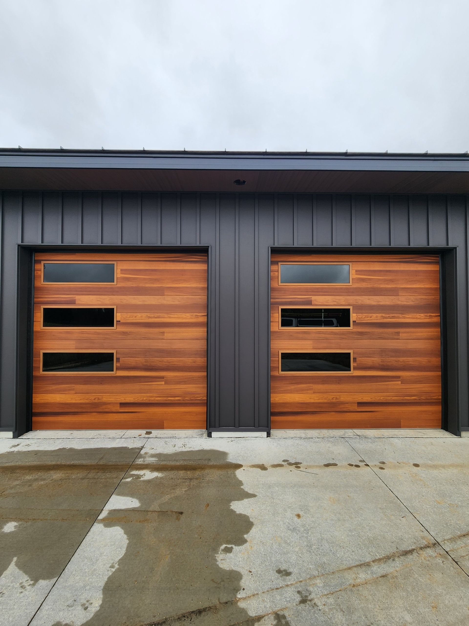 Two wooden garage doors with narrow windows on a dark modern house exterior