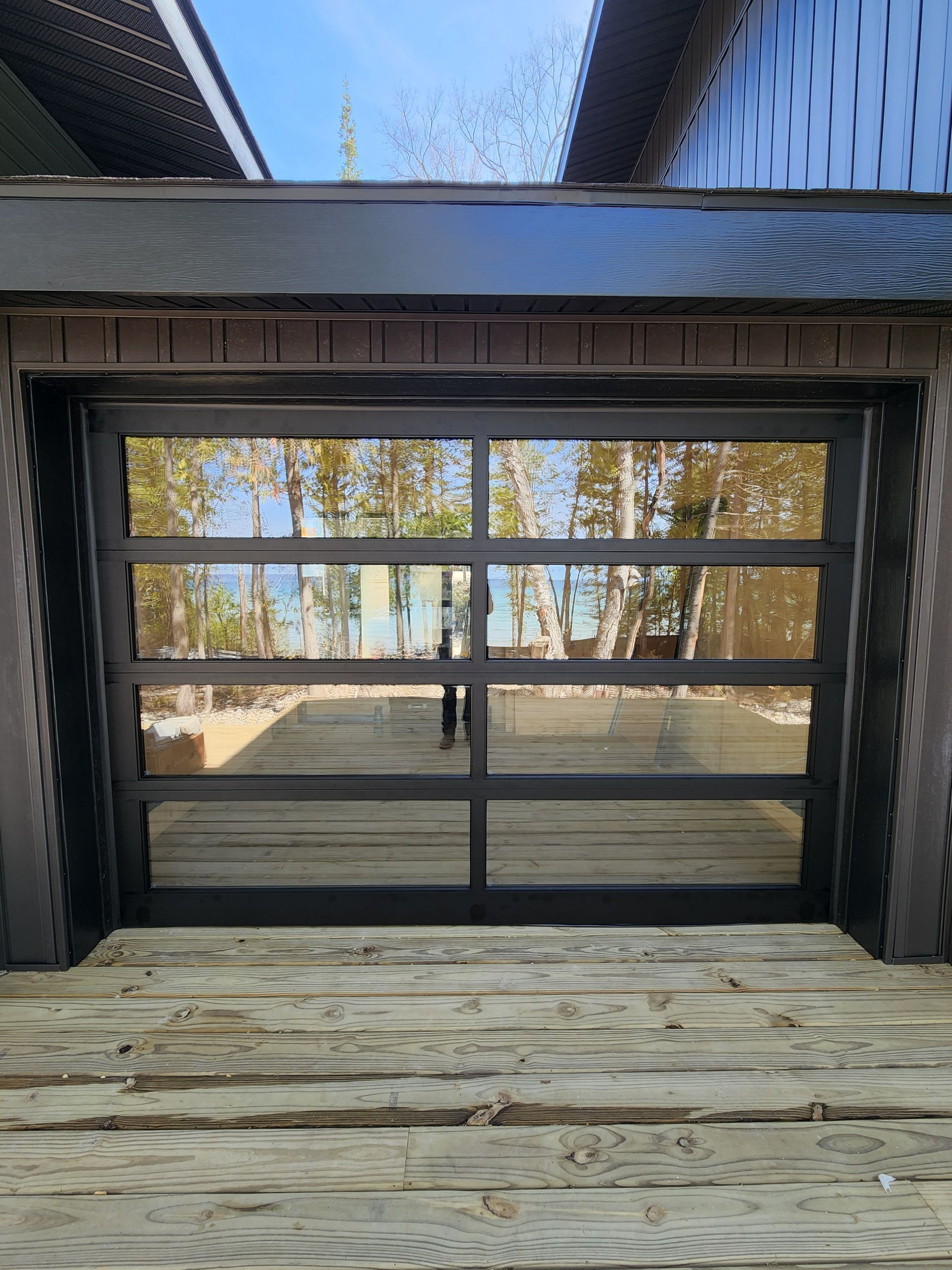 Wooden deck facing large black-framed sliding glass doors with trees and blue sky reflected in the glass