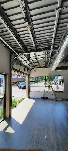Covered porch with exposed roof beams, gray floor, large windows, and a small table near an open side.
