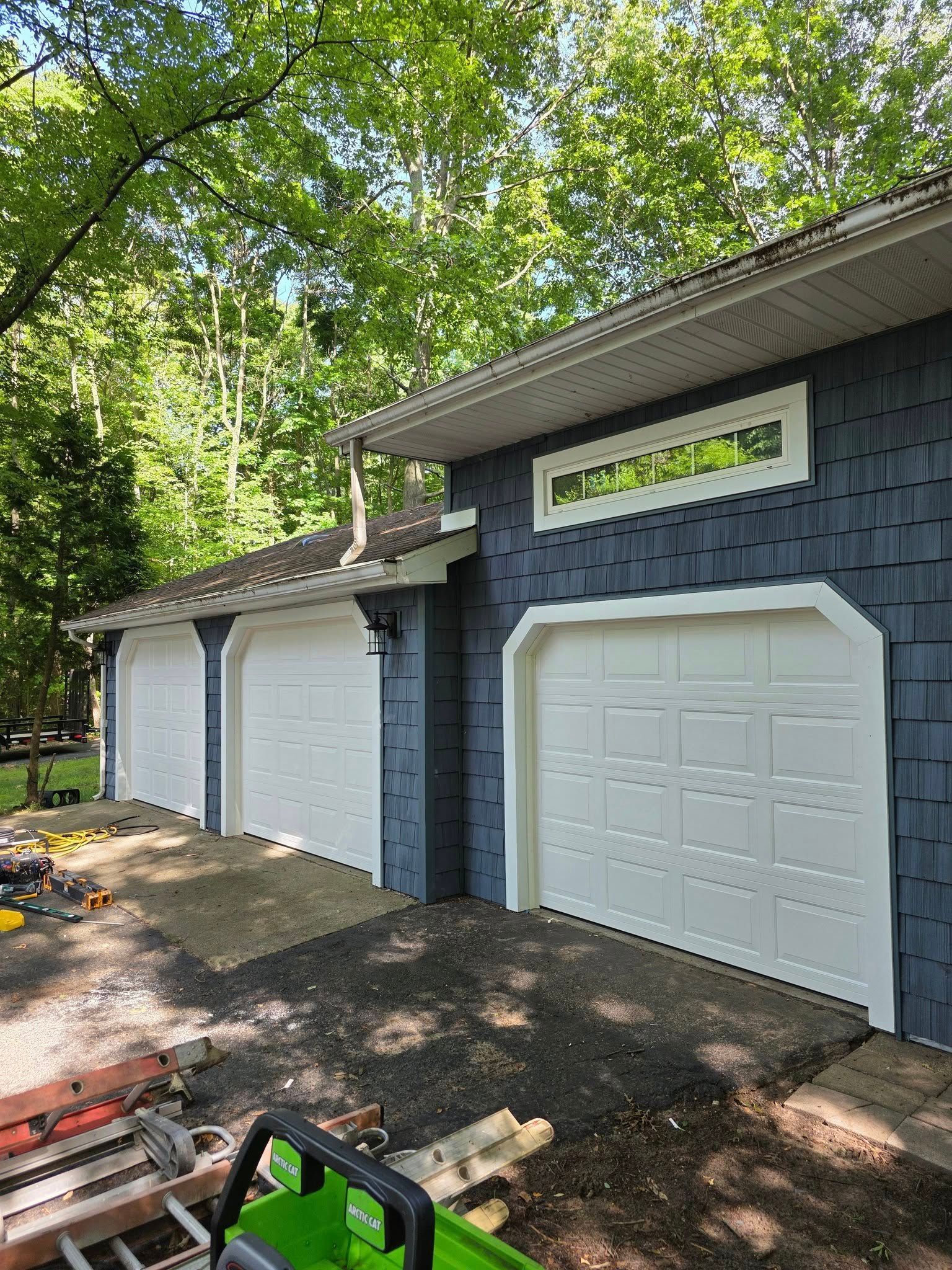 Three garage doors on a blue and white detached garage under trees