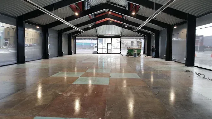 Empty industrial hall with polished concrete floor, exposed beams, and large windows at the far end
