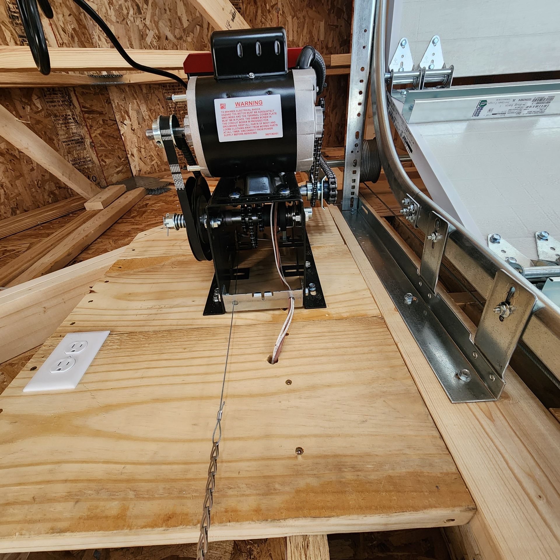 Black mechanical unit mounted on a wooden platform inside an unfinished attic or roof space.