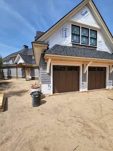 New house exterior with unfinished siding, front porch, and garage under construction.
