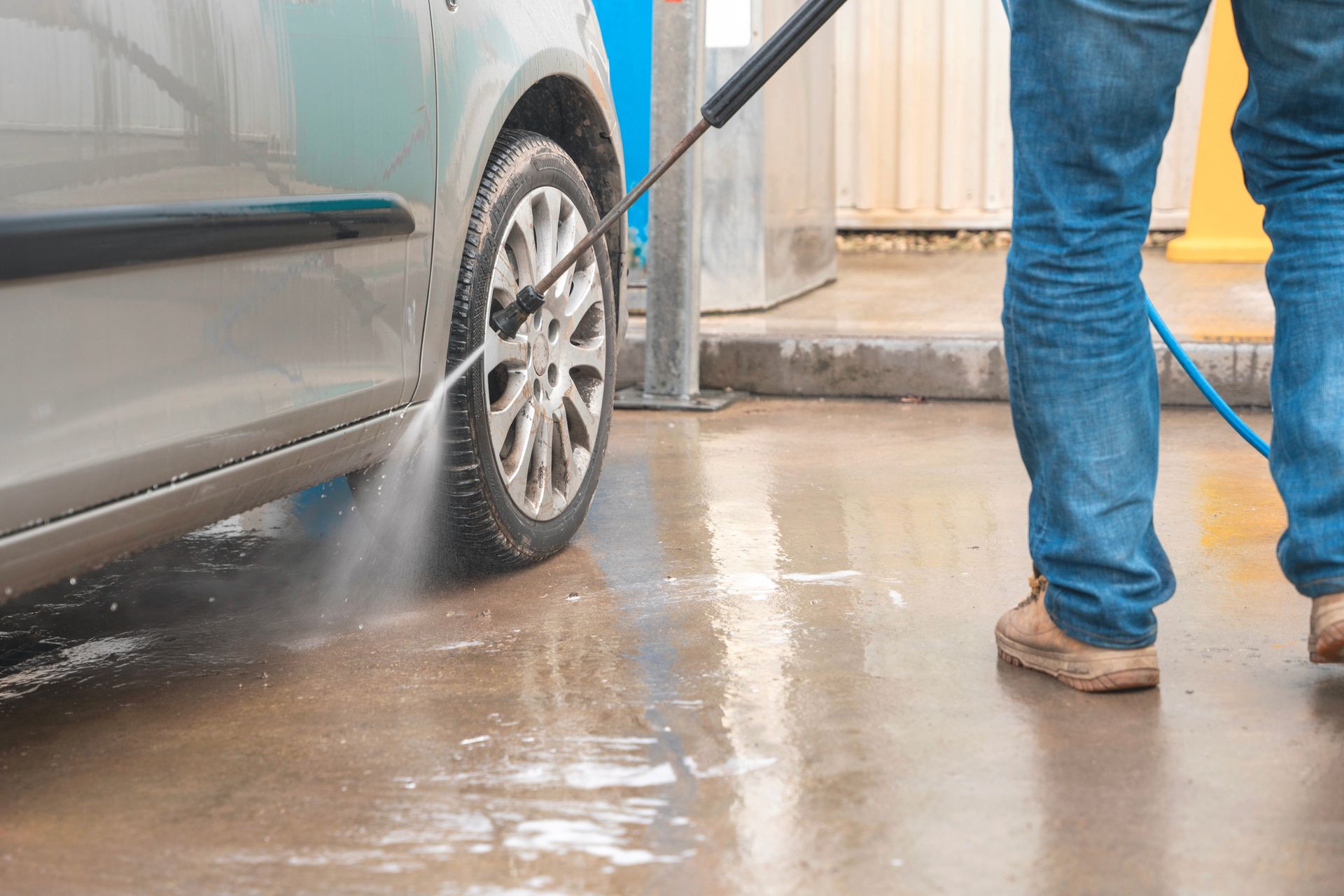 Person pressure-washing a car wheel on a wet driveway