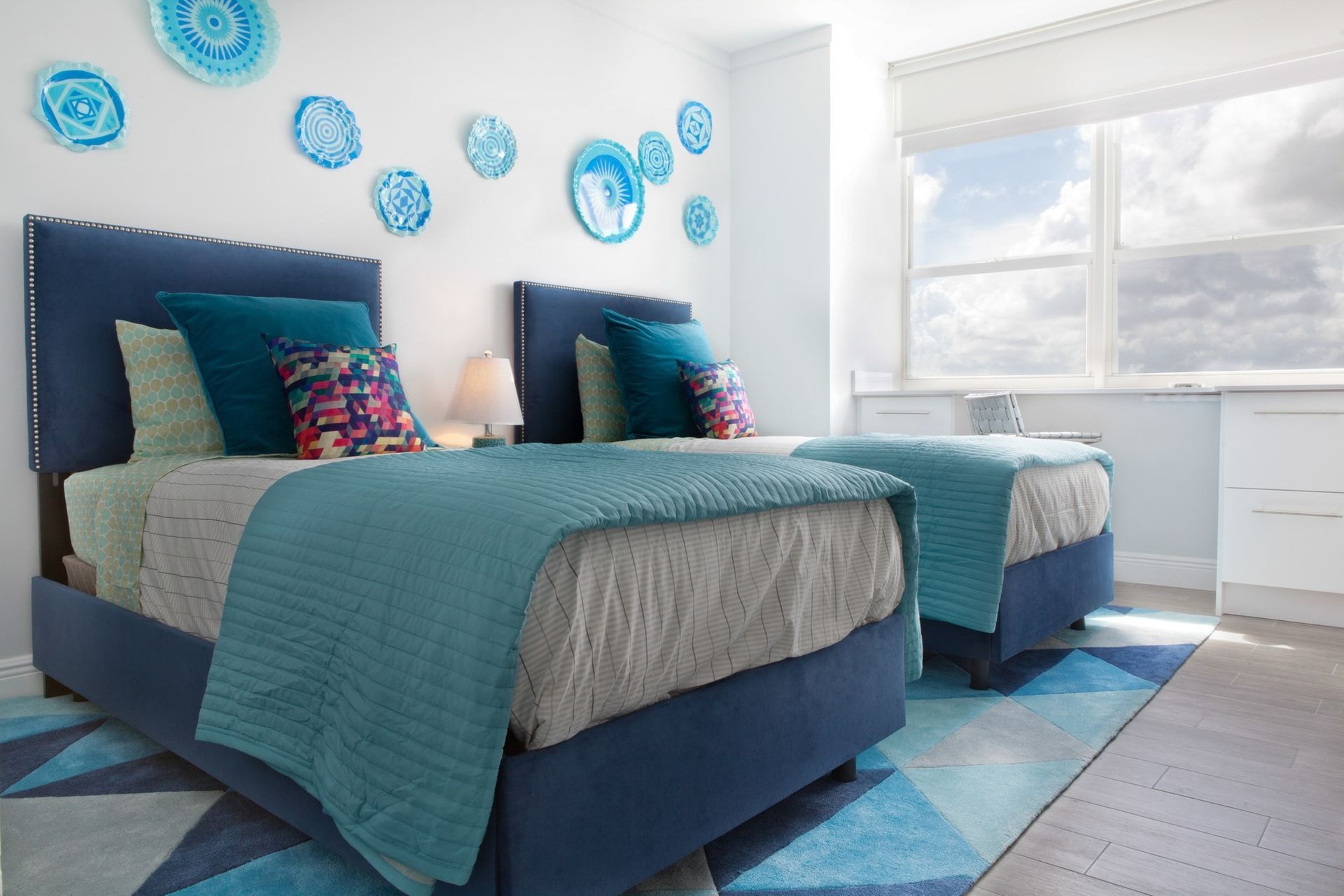 A bedroom with two beds and a window with blue plates on the wall.