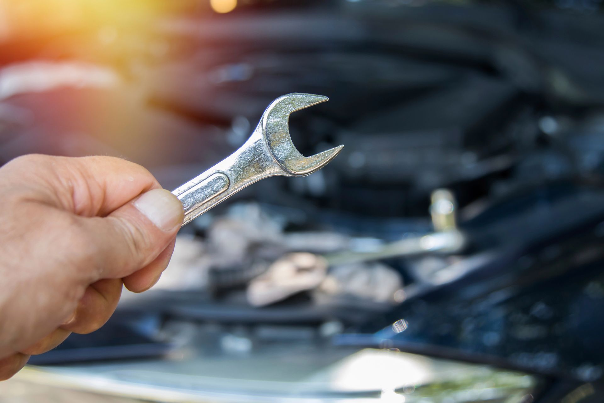 Una mano che impugna una chiave inglese davanti al vano motore aperto di un'auto.