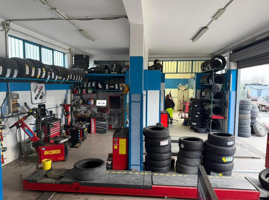 Officina meccanica con pneumatici impilati, sollevatori e attrezzature per l'equilibratura delle ruote all'interno di un garage.