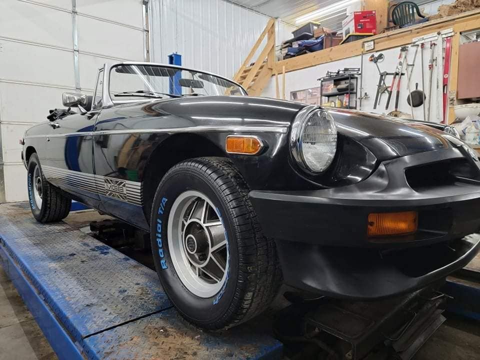 Black MG MGB convertible car on a lift in a garage.