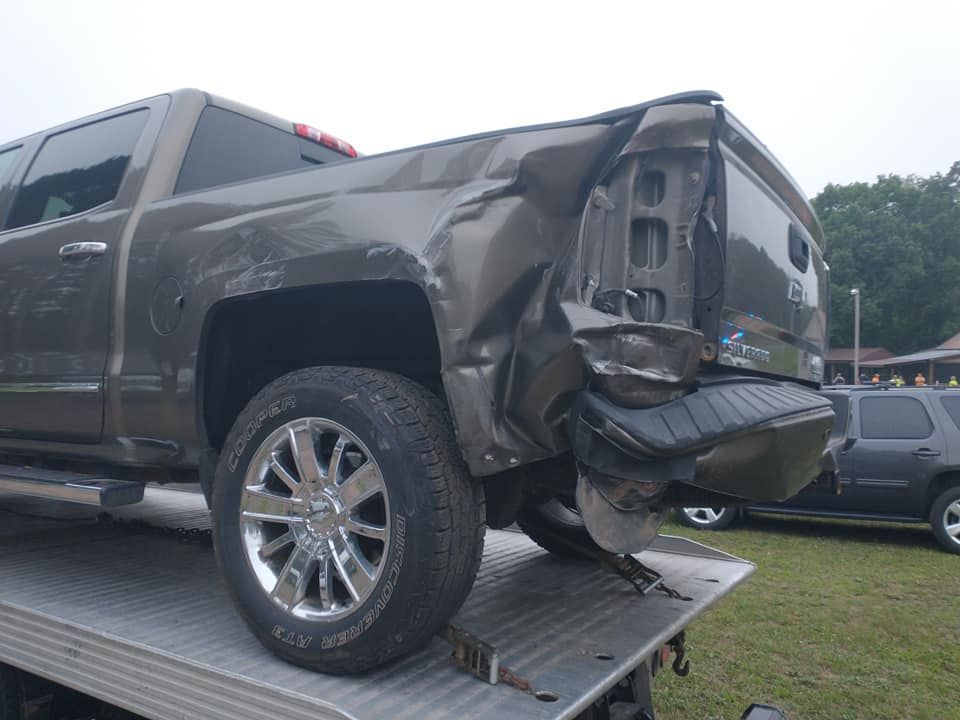 Damaged gray pickup truck on a tow truck. Rear end is heavily dented and the taillight is broken.