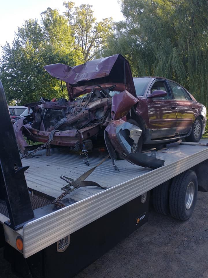 A badly damaged burgundy car loaded onto a flatbed tow truck.