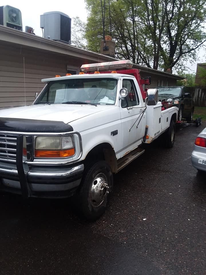 White tow truck parked in front of a house, towing a car.