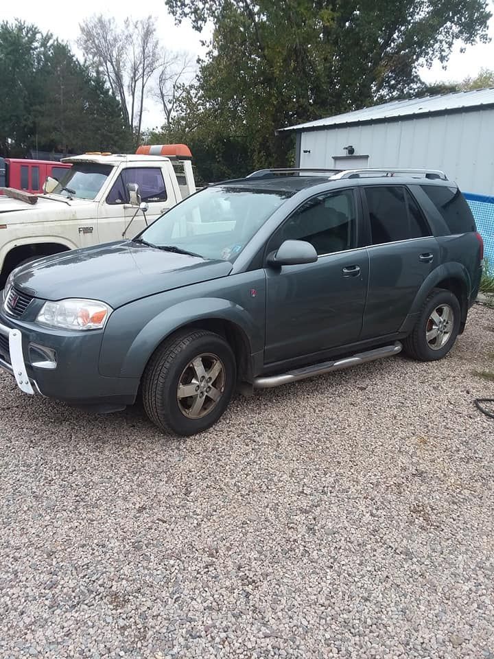 Dark gray Saturn SUV parked on gravel next to a white truck.