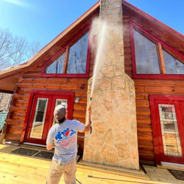 Person standing outside a red cabin with a stone chimney venting steam in bright sunlight