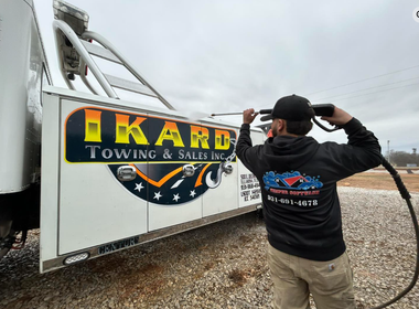 Person in black jacket salutes a large white tow truck with yellow TKD Towing & Salvage logo.