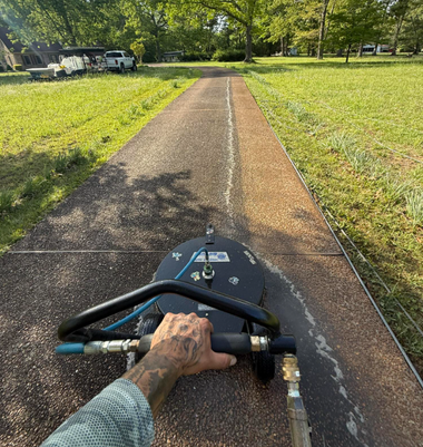 First-person view from a riding mower cutting a grassy park path in sunlight