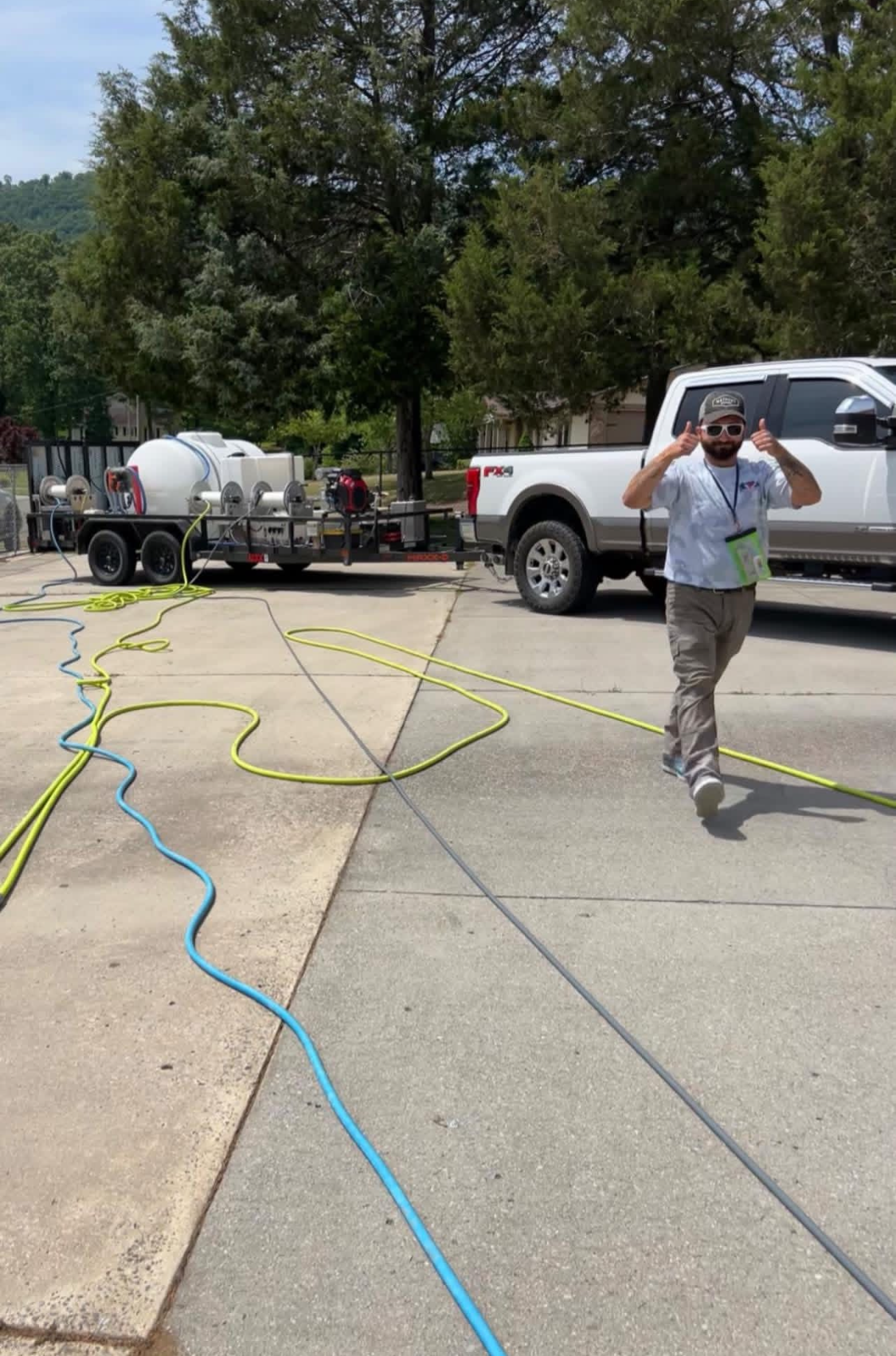 Worker walking near a white pickup truck and trailer with hoses stretched across a concrete lot
