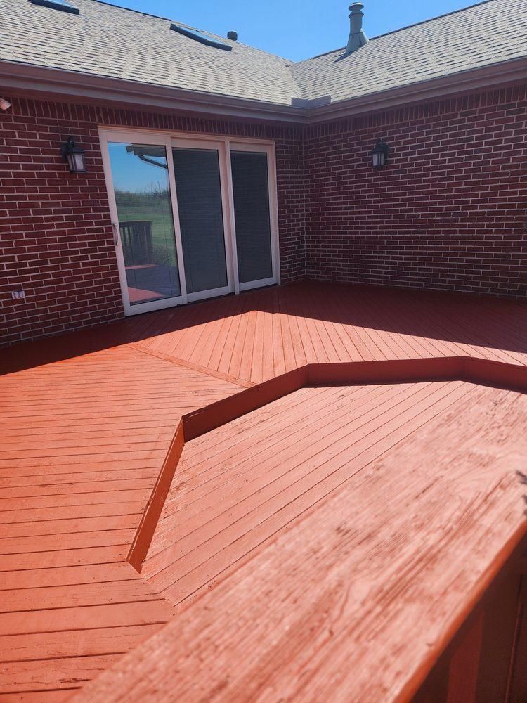 Backyard red wooden deck with raised section, brick walls, and sliding glass doors under bright sunlight
