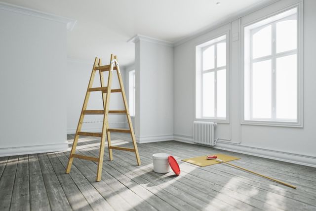 Bright empty room with a wooden ladder and painting supplies on the floor, near large windows.
