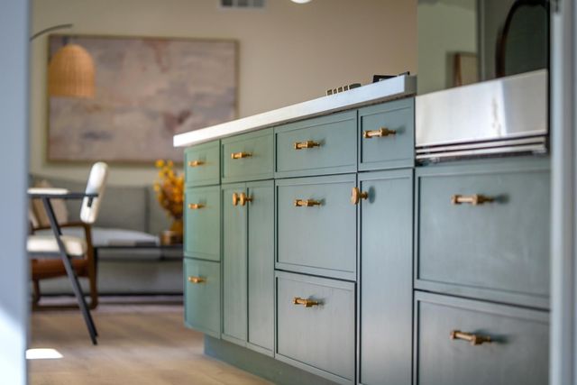 Mint-green kitchen cabinets with brass handles in a bright modern interior