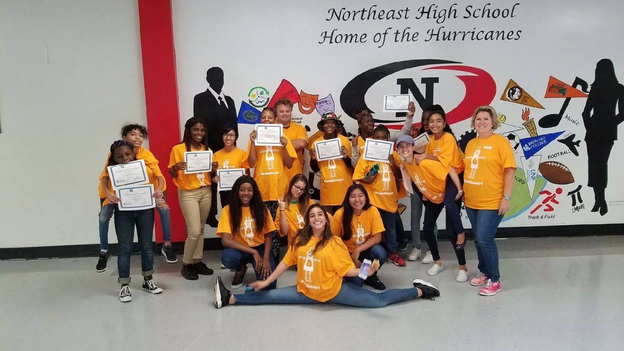 Group of students in orange shirts posing in a school hallway in front of a wall mural.