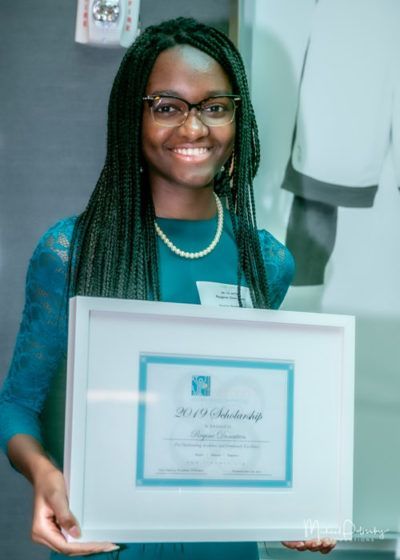 Woman with glasses smiling and holding a framed certificate in a bright indoor setting