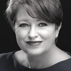 Black-and-white headshot of a smiling person with short hair, wearing a dark top.